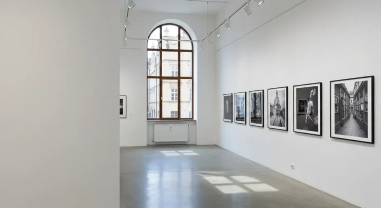Wnetrze krakowskiej galerii z rzedem oprawionych fotografii na bialej scianie i lukowym oknem z widokiem na kamienice st